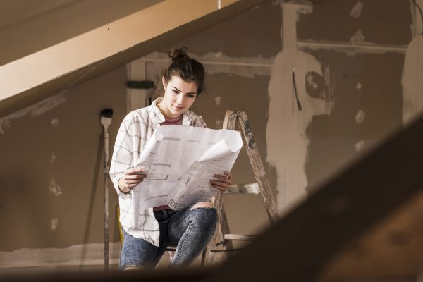 Young woman renovating her new home, holding construction plan